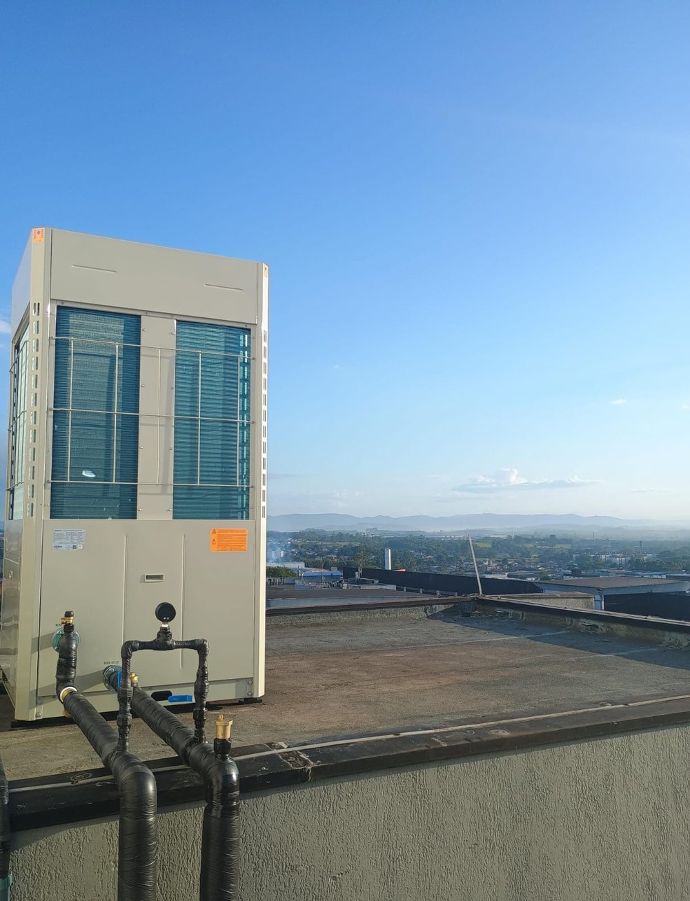 Bomba de calor instalada na cobertura de um edifício, com vista da cidade ao fundo.